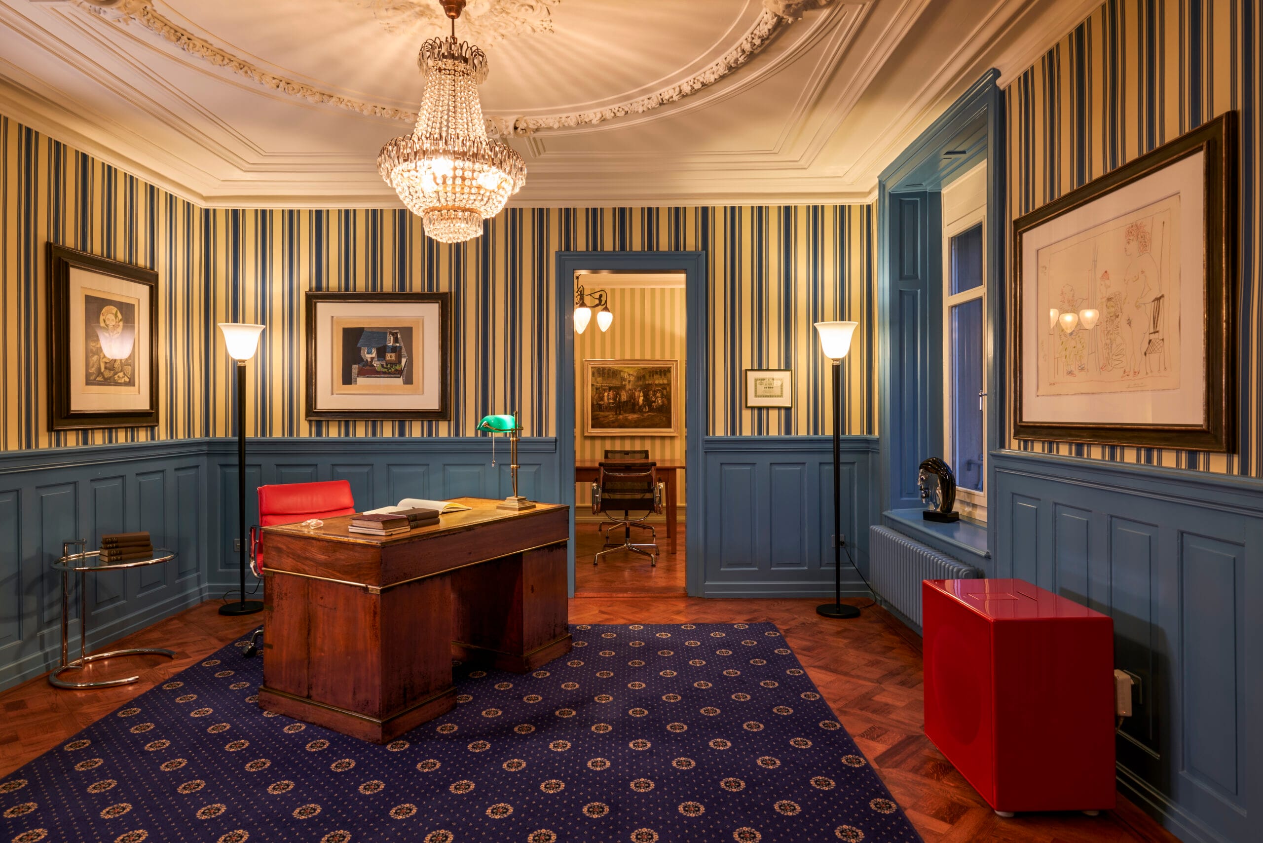 Salon Wohnzimmer mit elegantem Teppich, Holzschreibtisch und Kronleuchter in blau mit Streifentapete.