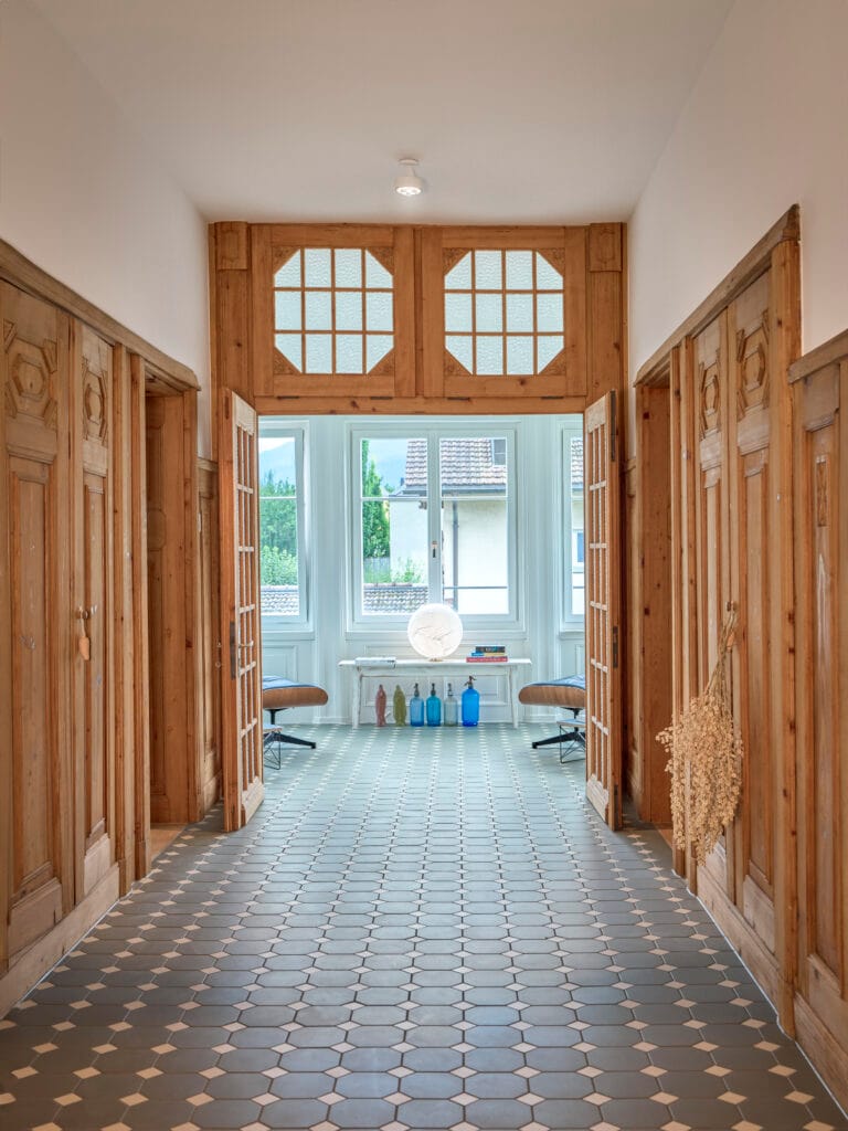 Schachbrettfliesen in lichtdurchflutetem Korridor mit Holztäfer und retro Einbauschränken mit gestämmten Türen. Traditionelle Schweizer Architektur